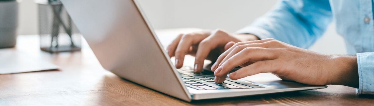 Hände einer Person sind zu sehen, wie sie etwas in einen Laptop tippen