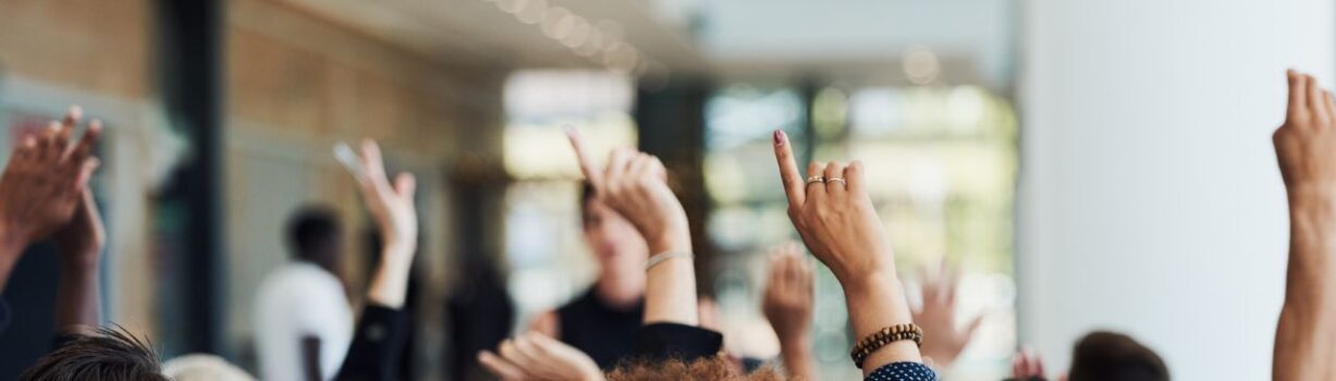 Ausschnitt einer Gruppe von Personen, die sich melden