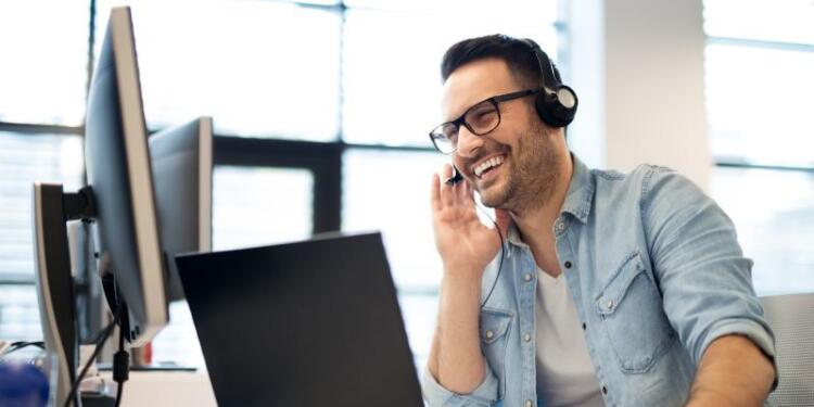 Ein Servicemitarbeiter mit Headset sitzt lächelnd vor einem Bildschirm