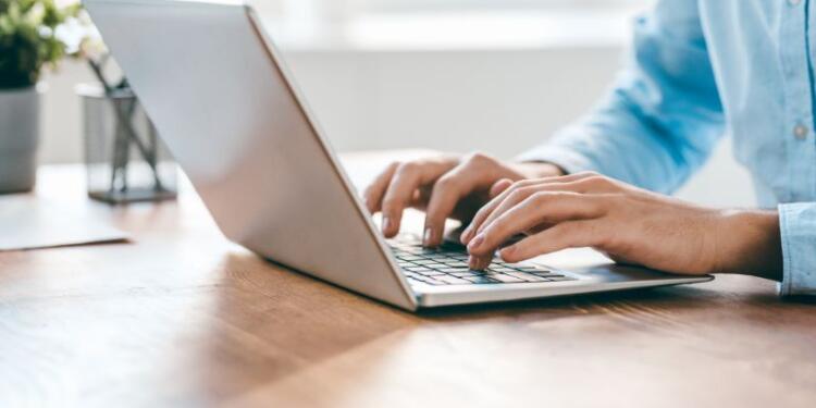 Hände einer Person, wie sie etwas in einen Laptop tippen