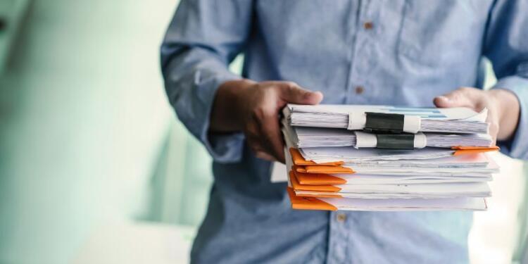 Ein Mann, der einen Stapel Unterlagen trägt; der Hintergrund ist verschwommen