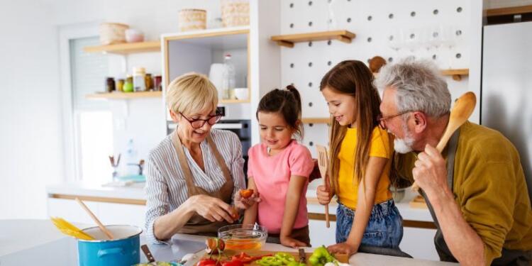 Vierköpfige Familie mit Großeltern und zwei Enkelinnen bereitet gemeinsam eine Mahlzeit vor