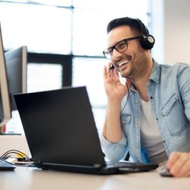 Ein Servicemitarbeiter mit Headset sitzt lächelnd vor einem Bildschirm
