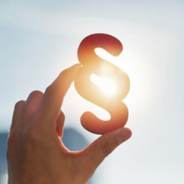 Eine Hand, die auf einen Rechtsparagrafen zeigt, der gegen die Sonne gehalten wird