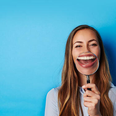 Junge Frau hält eine Lupe vor ihren Mund, der dadurch stark vergrößert erscheint