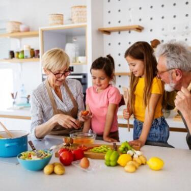 Vierköpfige Familie mit Großeltern und zwei Enkelinnen bereitet gemeinsam eine Mahlzeit vor